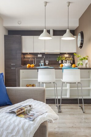 A modern kitchen with white cabinets, a central island, pendant lighting, and a dining area with white chairs. - Absynt Apartments Old Town Deluxe (Wroclaw)