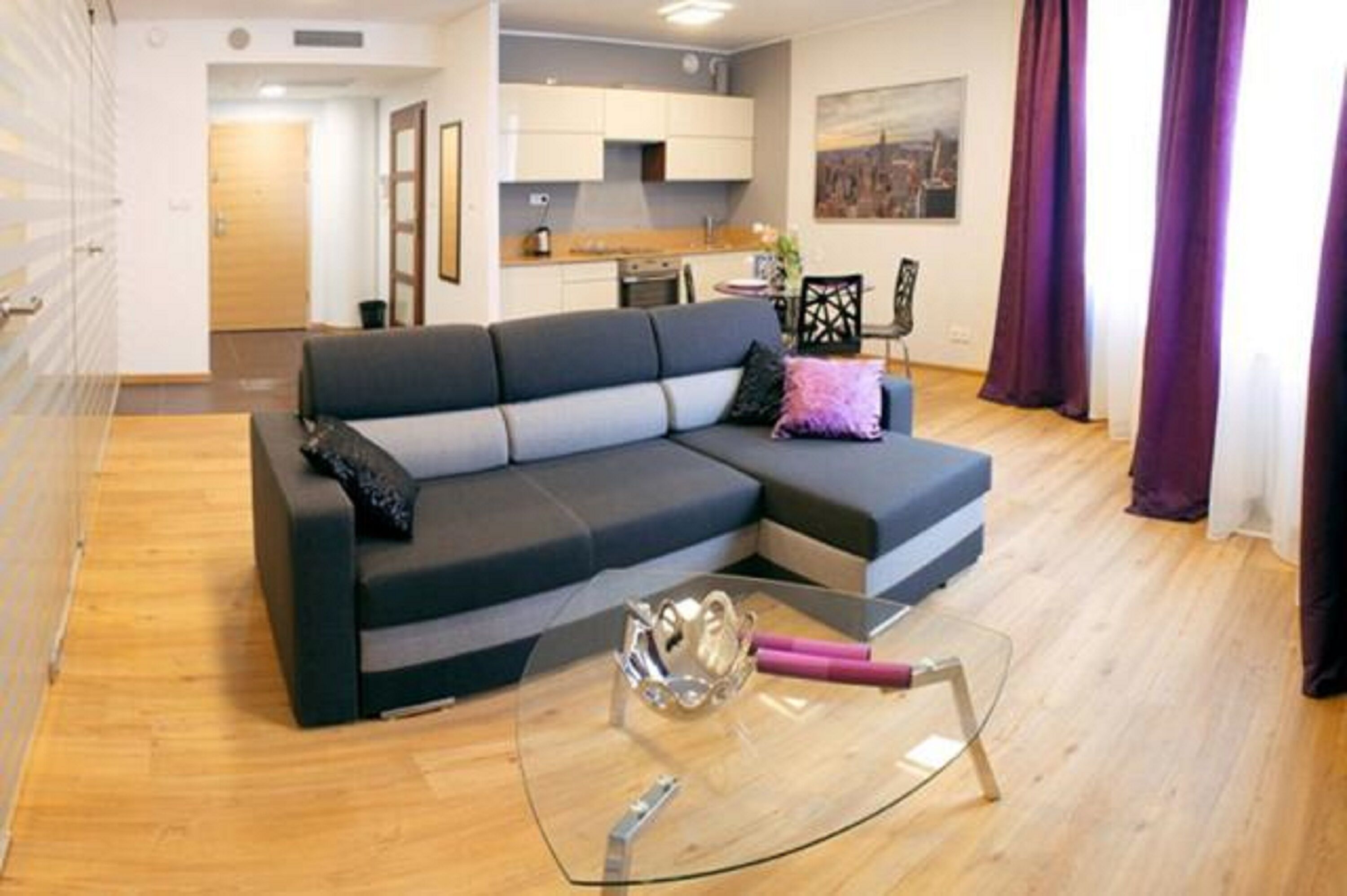 A modern living room with a sectional sofa, a glass coffee table, and a kitchen in the background.