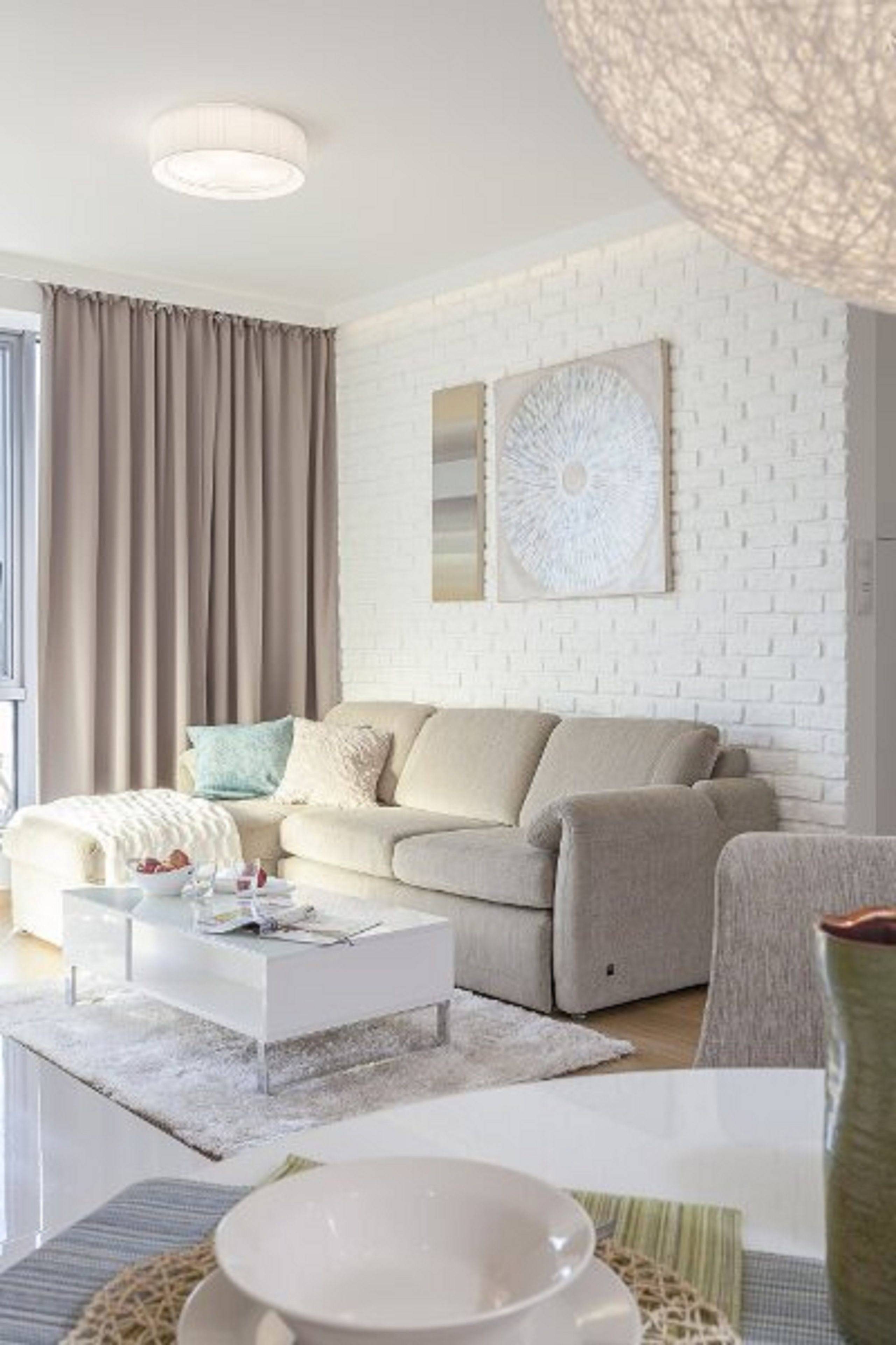 A modern living room with a white brick wall, a beige sofa, a coffee table, and a large abstract painting.