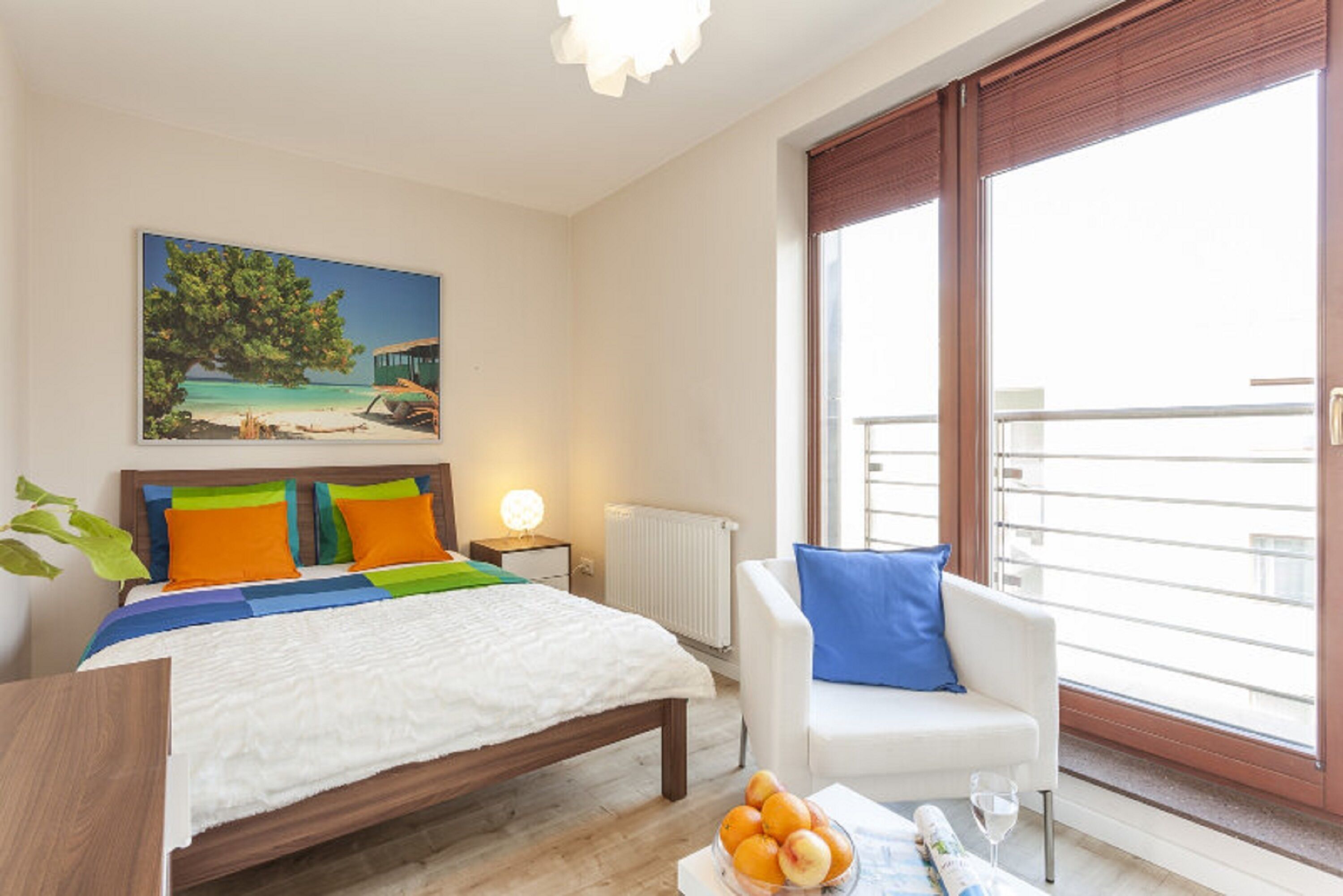 Quarto com cama, mesa de cabeceira, cadeira e janela com vista para o exterior.