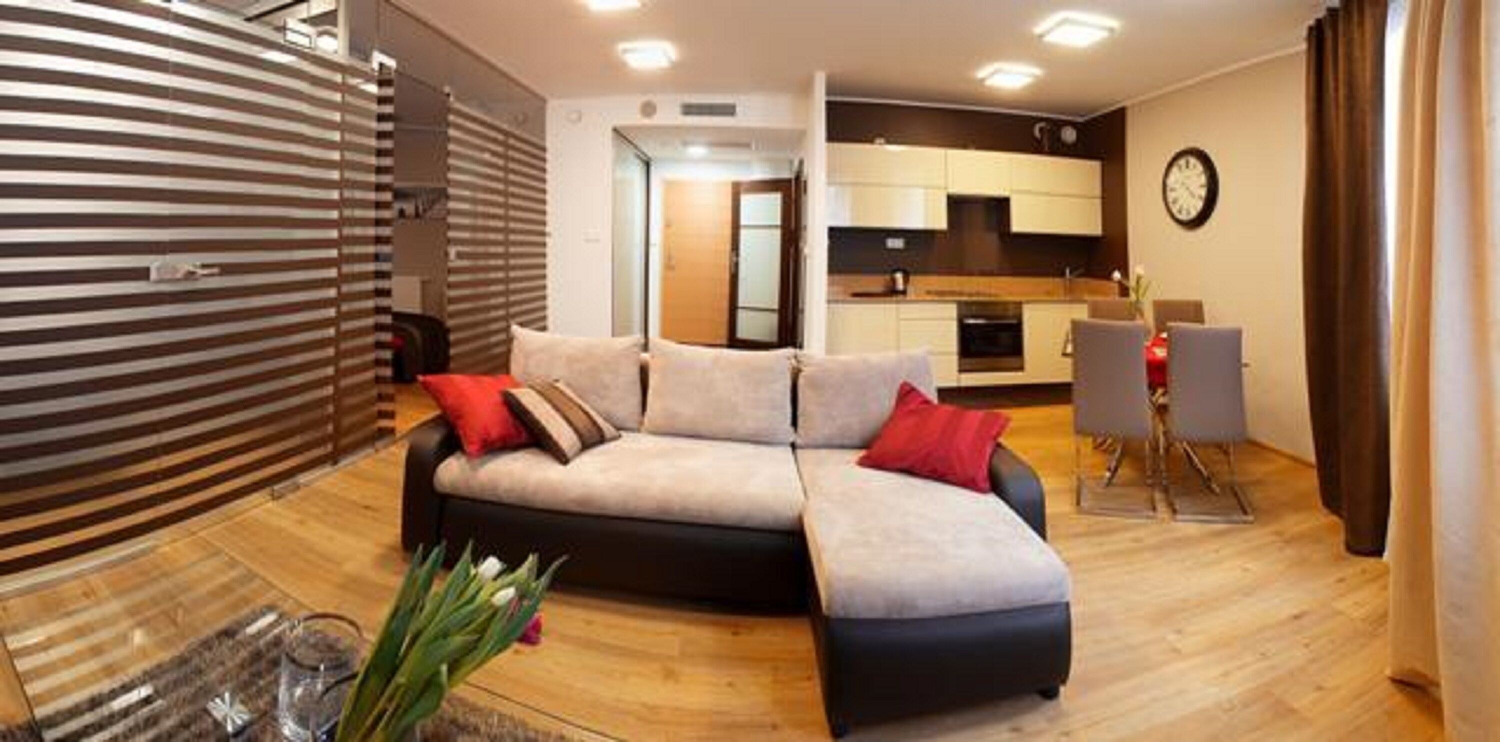 A modern living room with a sectional sofa, a dining area with a table and chairs, and a kitchen in the background.