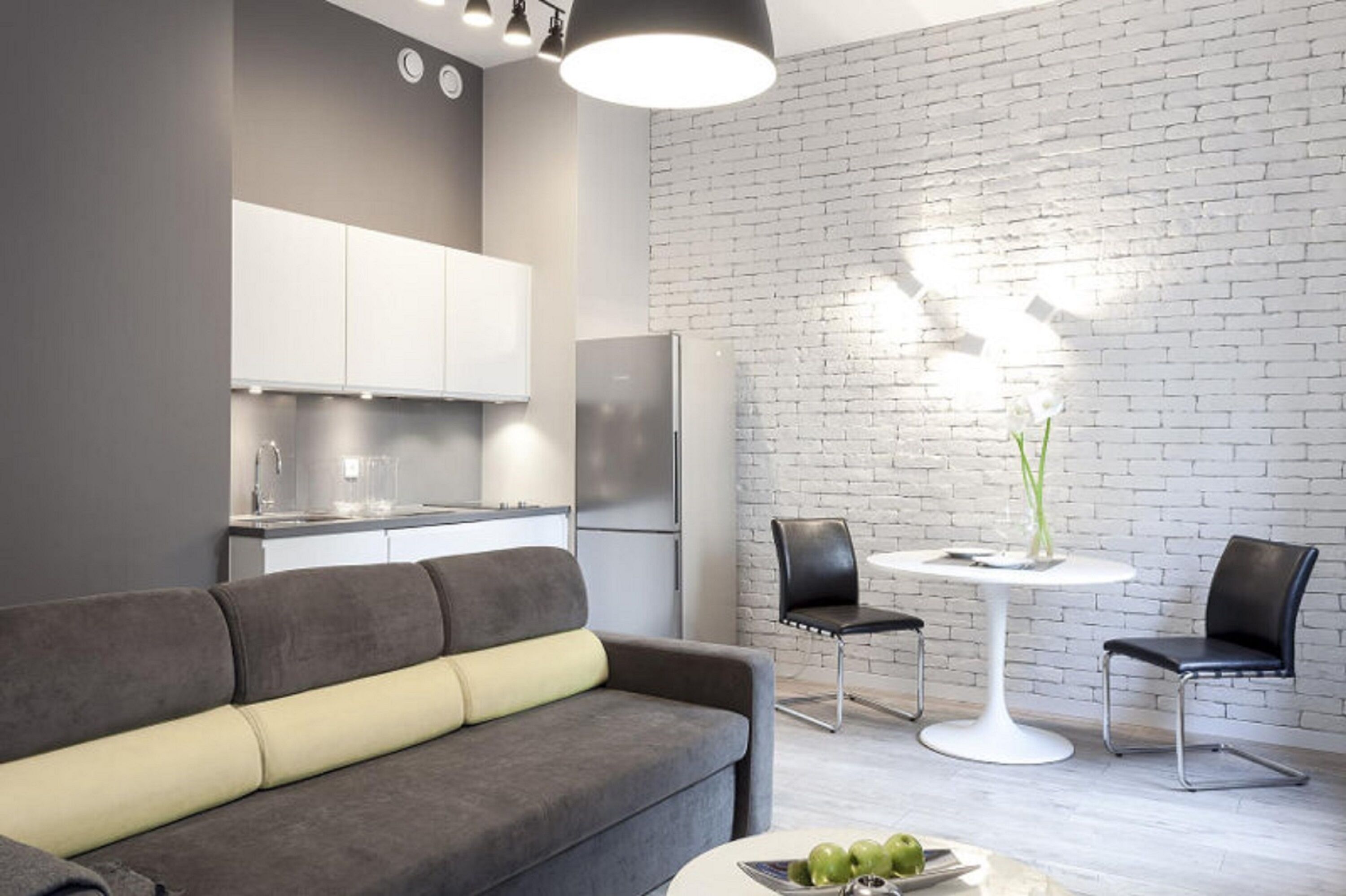 Un salón moderno con un sofá gris, una mesa redonda blanca y dos sillas negras.