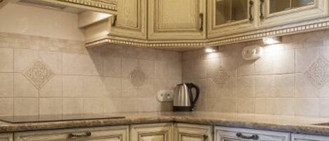 A kitchen with light-colored cabinetry, a stove, and a kettle on the countertop.