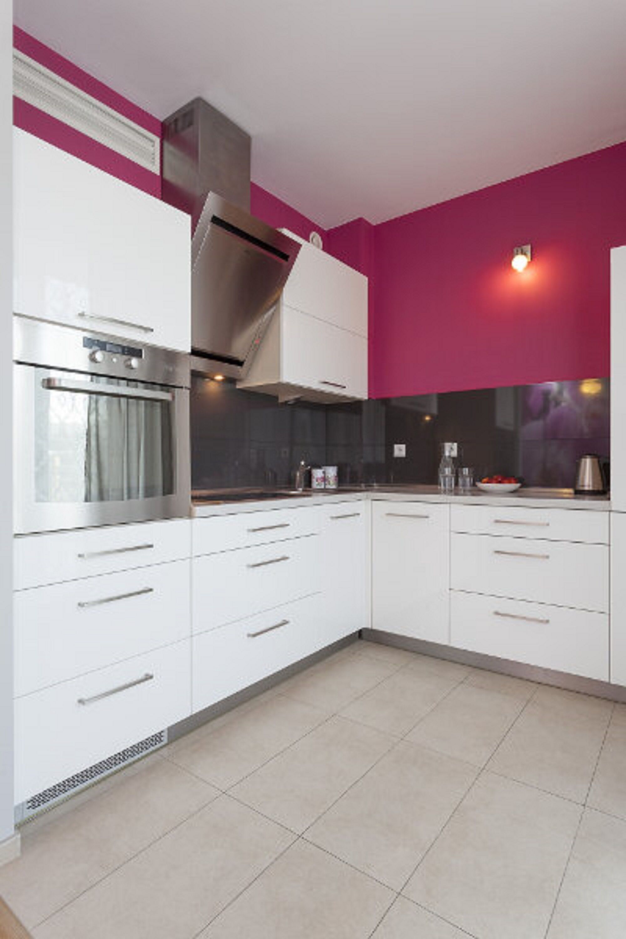 Une cuisine moderne avec des meubles blancs, une hotte en acier inoxydable et un mur d’accent rouge.