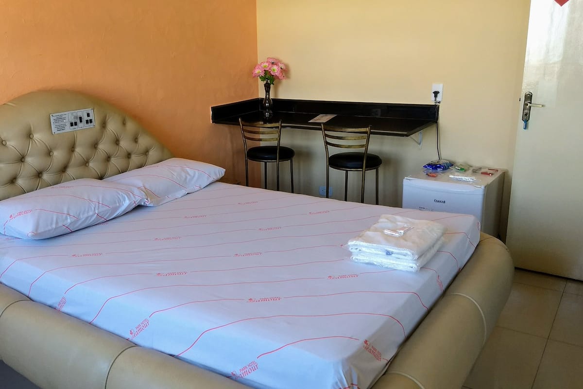 A hotel room with a bed, a small desk, two chairs, a vase with flowers, and a door.