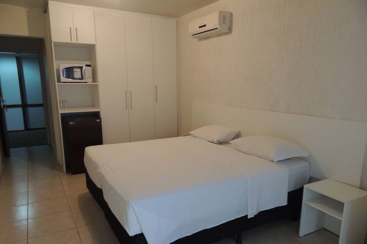 Un dormitorio con cama, mesita de noche, armario y microondas.