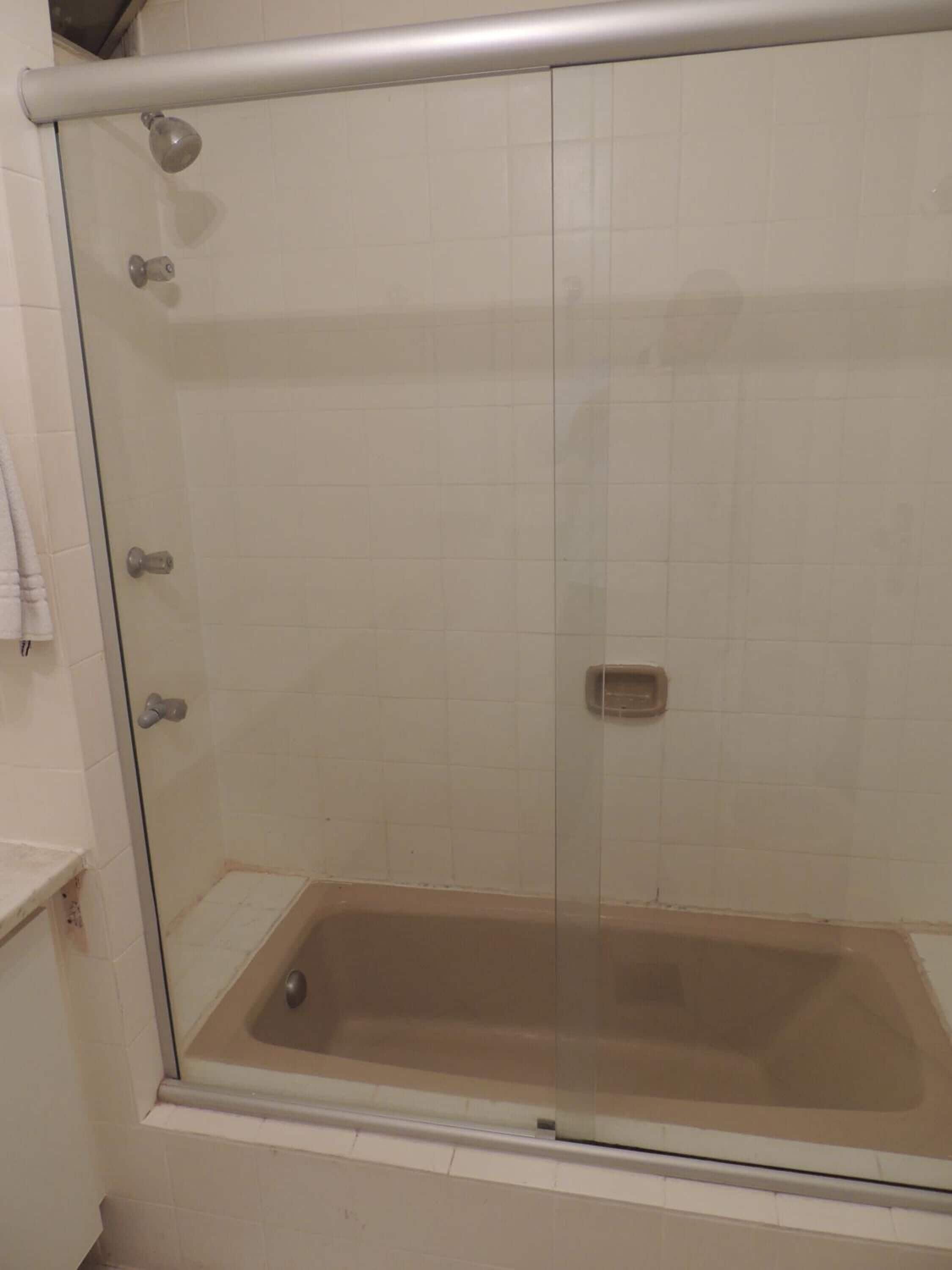 A glass-enclosed shower stall with a bathtub, white tiled walls, and a metal showerhead.