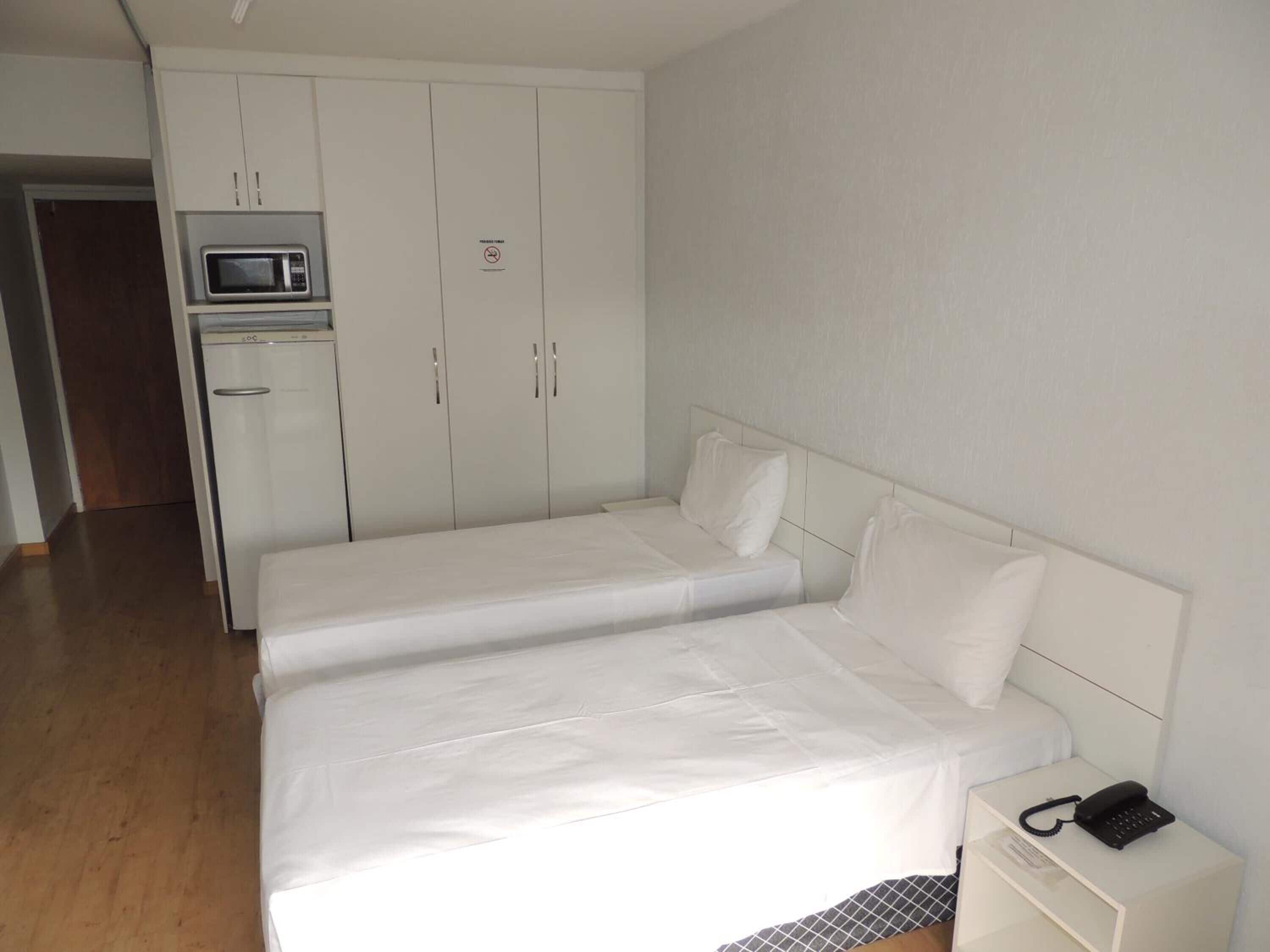 A small, clean room with two single beds, a white wardrobe, a microwave, and a bedside phone.