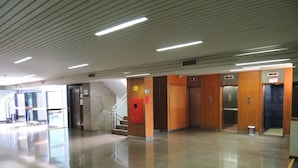 A spacious lobby with a polished floor, a staircase, and multiple elevators.