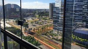 A view from a high-rise window overlooking a parking lot, a road, and modern buildings.