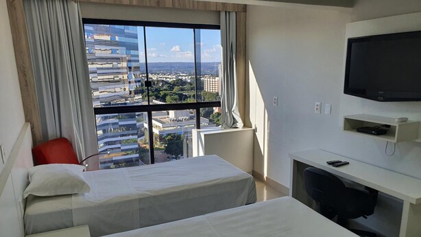 A hotel room with two beds, a desk, a chair, a TV, and a view of the cityscape.