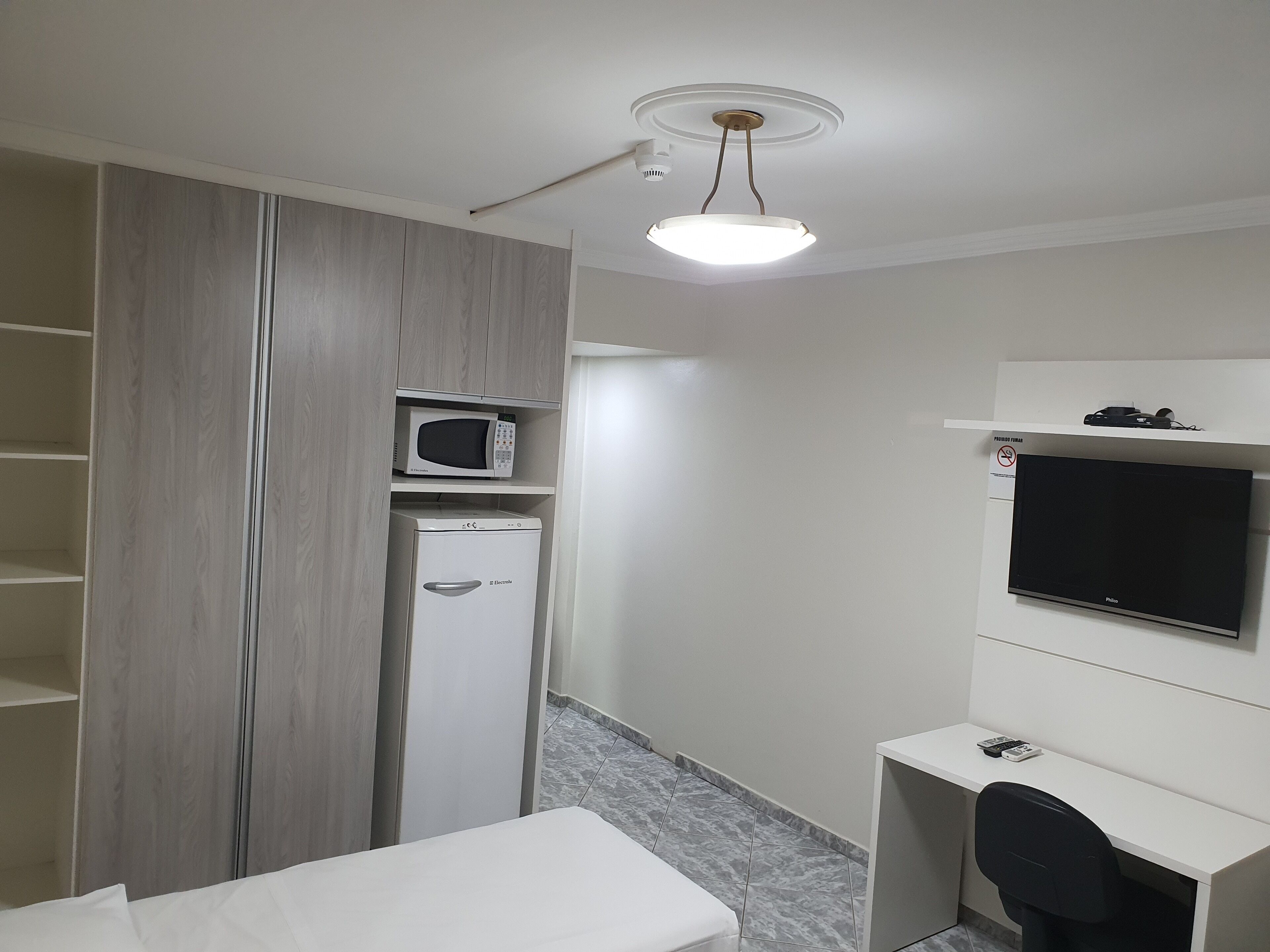 Una camera d'albergo con un letto, una scrivania, un forno a microonde, un frigorifero e una televisione.