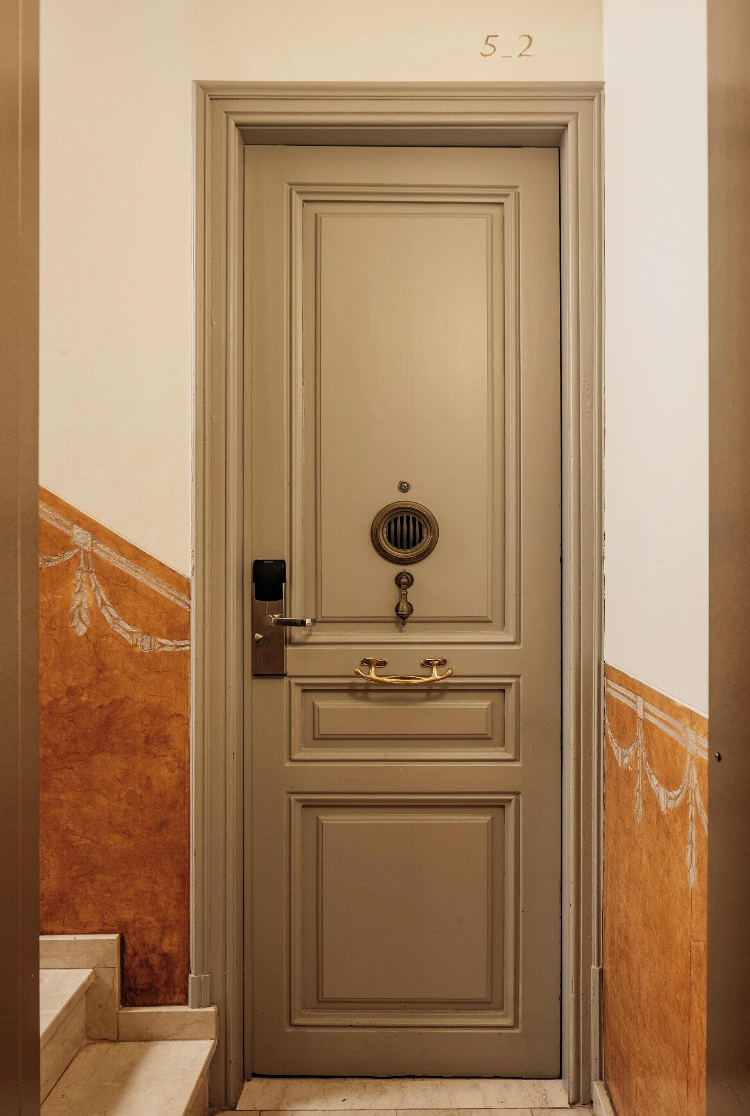 A closed door with a brass handle and a keyhole, a small window with a grille, and a number "5-2" above it.