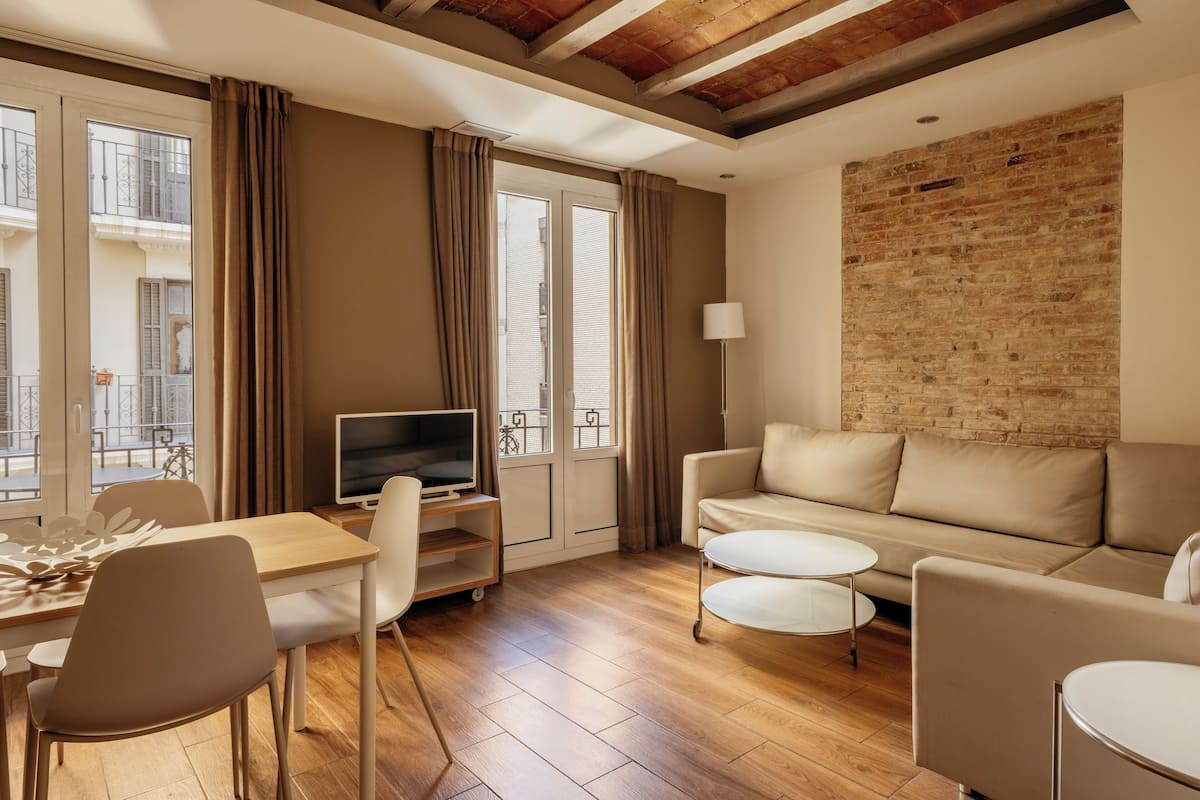 Un salon moderne avec un plancher en bois, un canapé beige, un téléviseur posé sur un meuble et un mur en briques.
