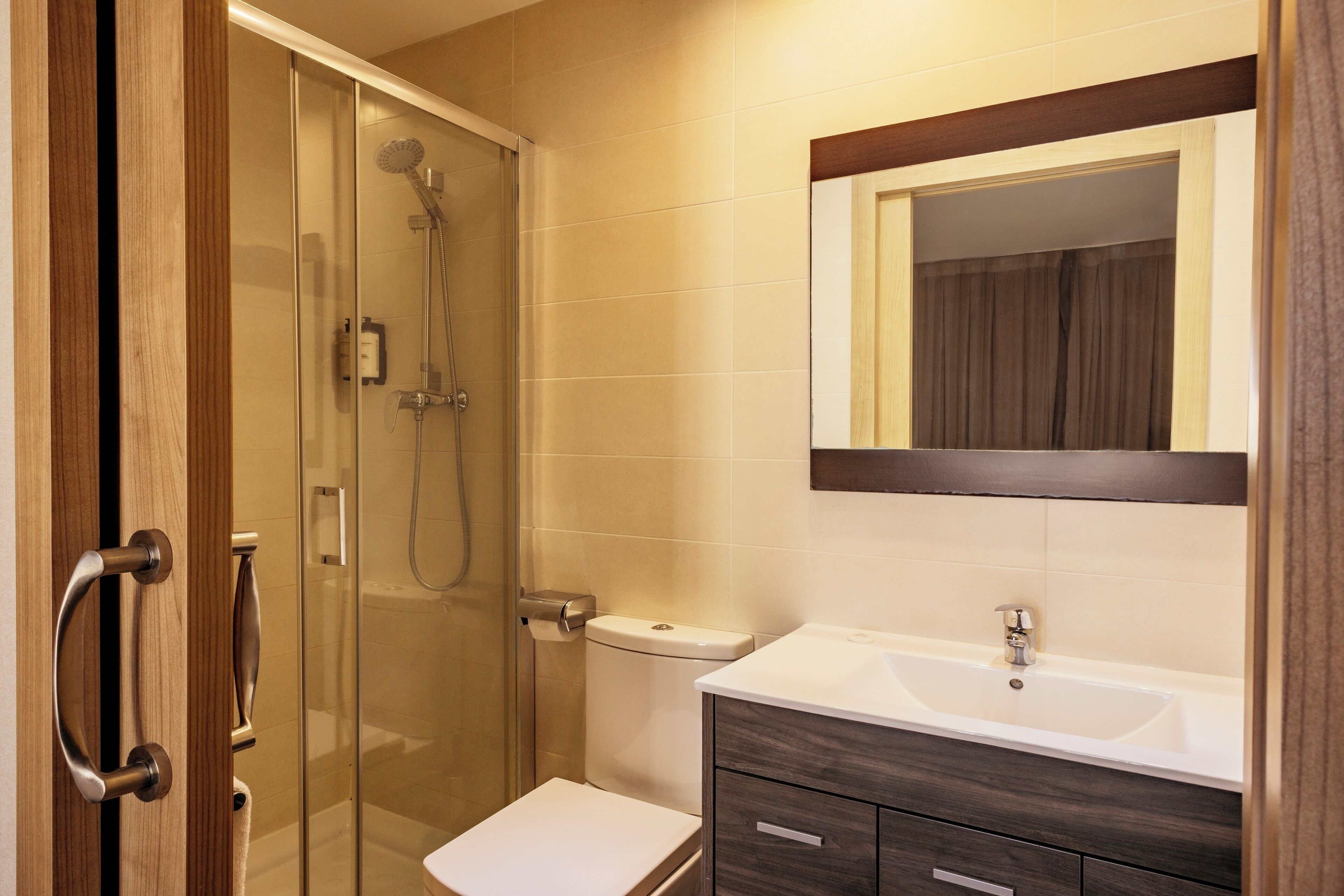 A bathroom with a glass shower enclosure, a toilet, a sink with a mirror above it, and wooden cabinetry.
