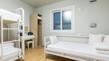 A bunk bed room with a desk and wardrobe, a single bed with pillows, and a window with blinds.