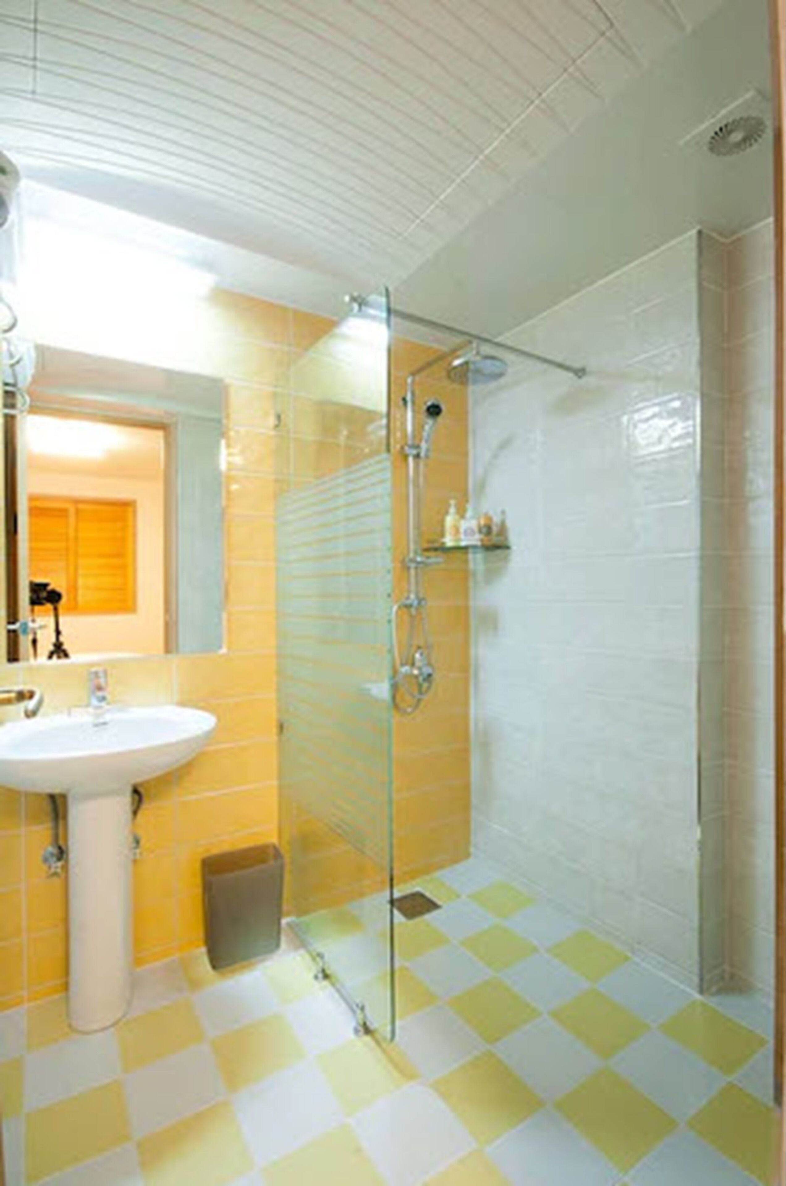 A bathroom with a glass shower enclosure, a sink, and yellow checkered flooring.
