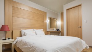 A neatly made bed with white bedding, a wooden headboard, a bedside table with a lamp, and a mirror above it. - Uniqstay (Busan)