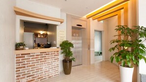 A modern hotel lobby with a reception desk, a brick accent wall, a potted plant, and a wooden-framed elevator. - Uniqstay (Busan)