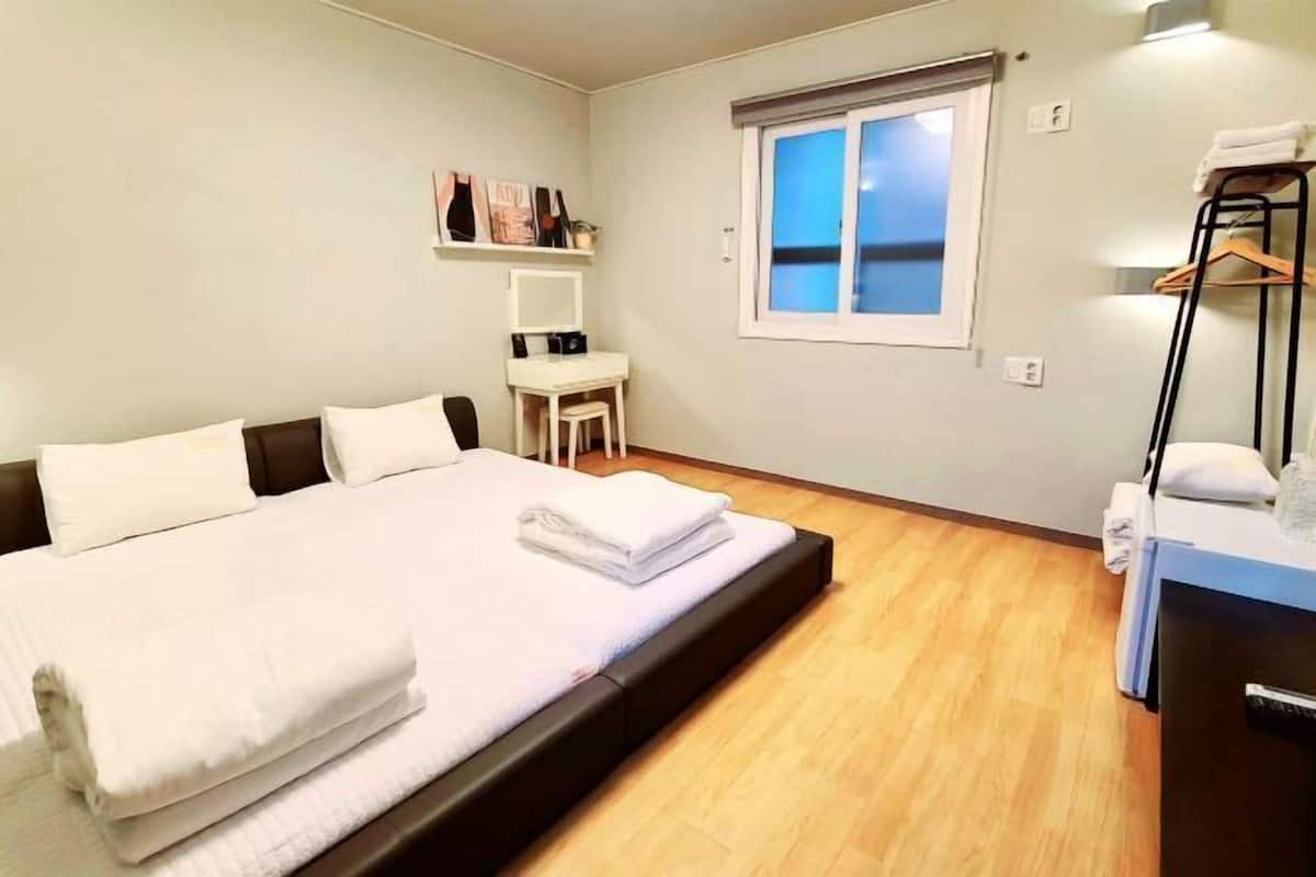 A bedroom with a bed, a desk, a chair, a window, and a wardrobe.