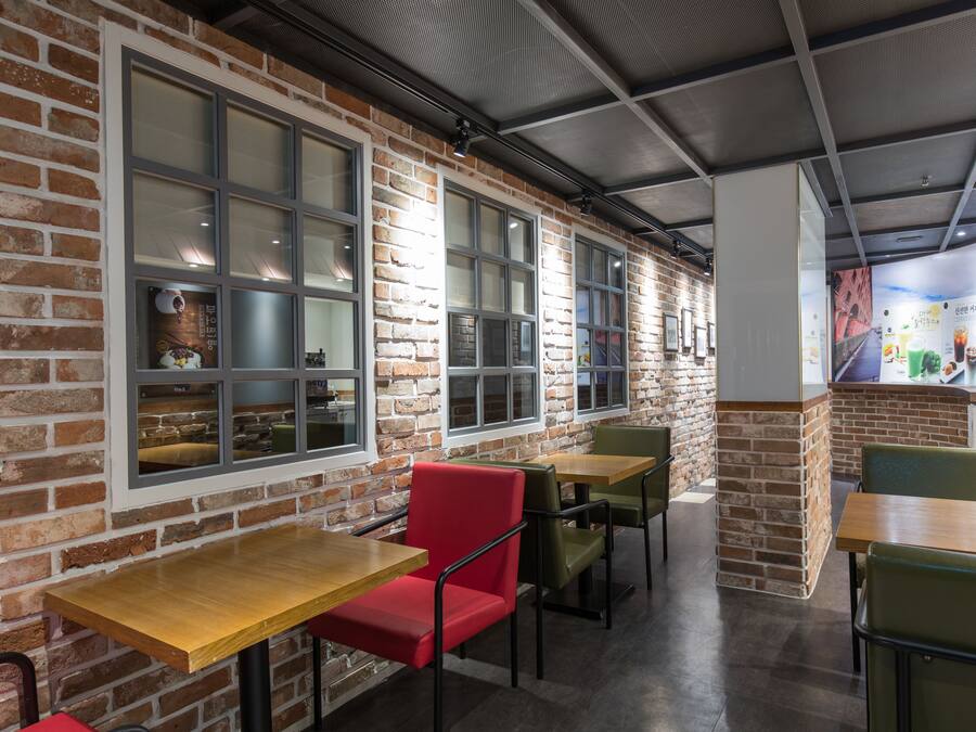 A restaurant interior with brick walls, large windows, and wooden tables and chairs.