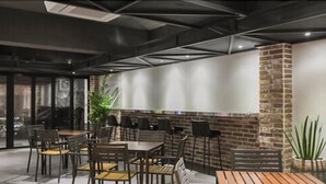 A modern indoor dining area with brick walls, multiple tables and chairs, and a large window providing a view of the city. - Uniqstay (Busan)