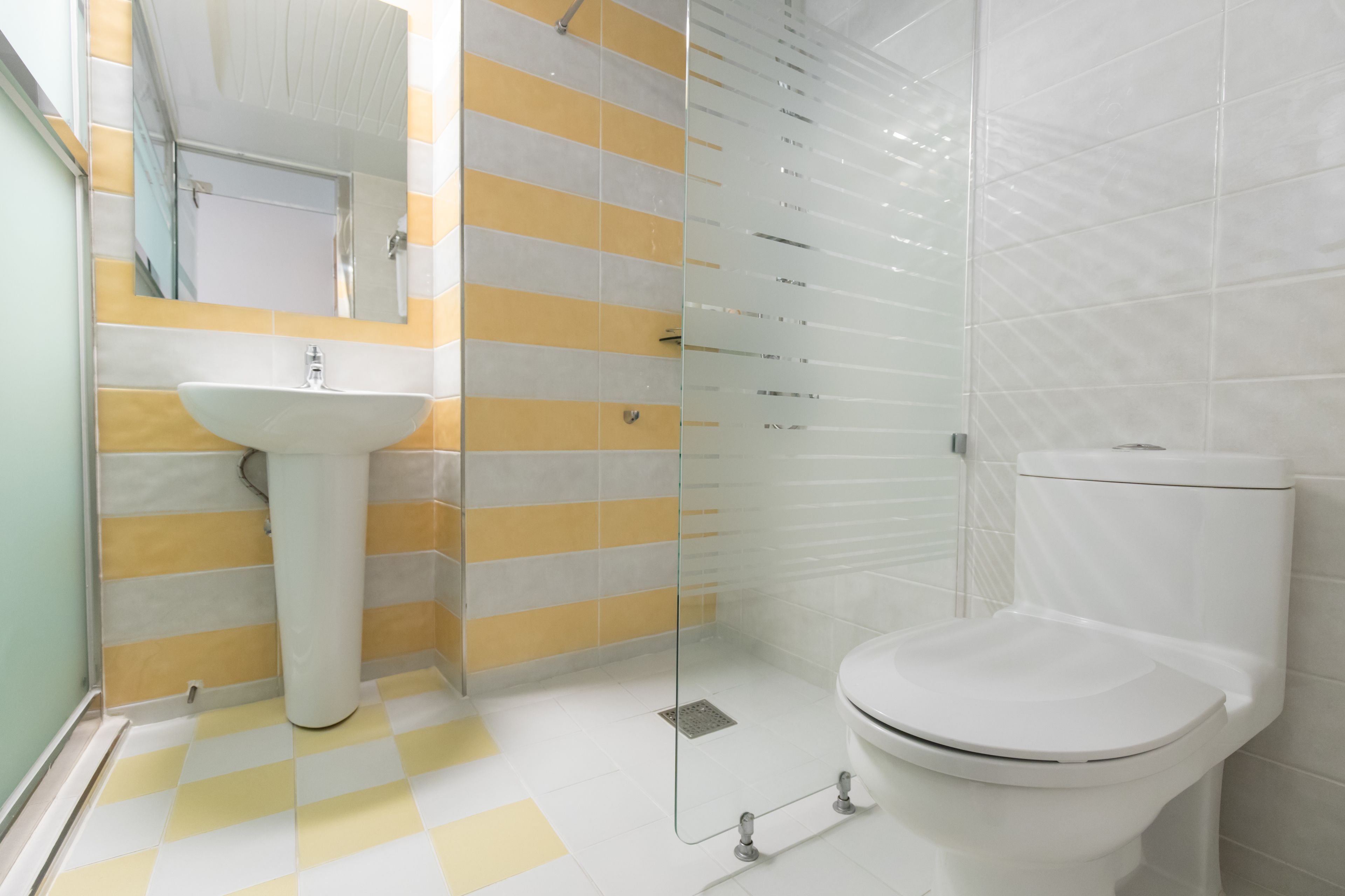 Un baño con un lavamanos blanco, paredes a rayas amarillas y blancas, una cabina de ducha de vidrio y un inodoro blanco.