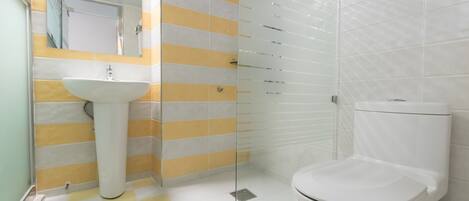 Un baño con un lavamanos blanco, paredes a rayas amarillas y blancas, una cabina de ducha de vidrio y un inodoro blanco.