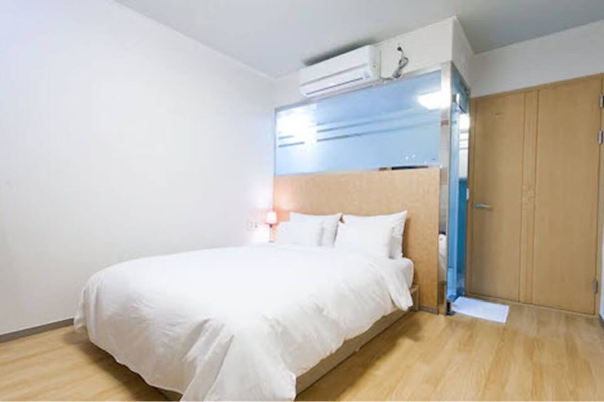 A bedroom with a bed, wooden flooring, a wardrobe, and an air conditioning unit.
