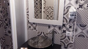 Casa de banho com azulejos estampados, pia, espelho e secador de cabelo.