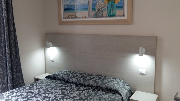 Quarto com cama, duas mesas de cabeceira, um criado-mudo, um quadro na parede e uma janela com cortinas.