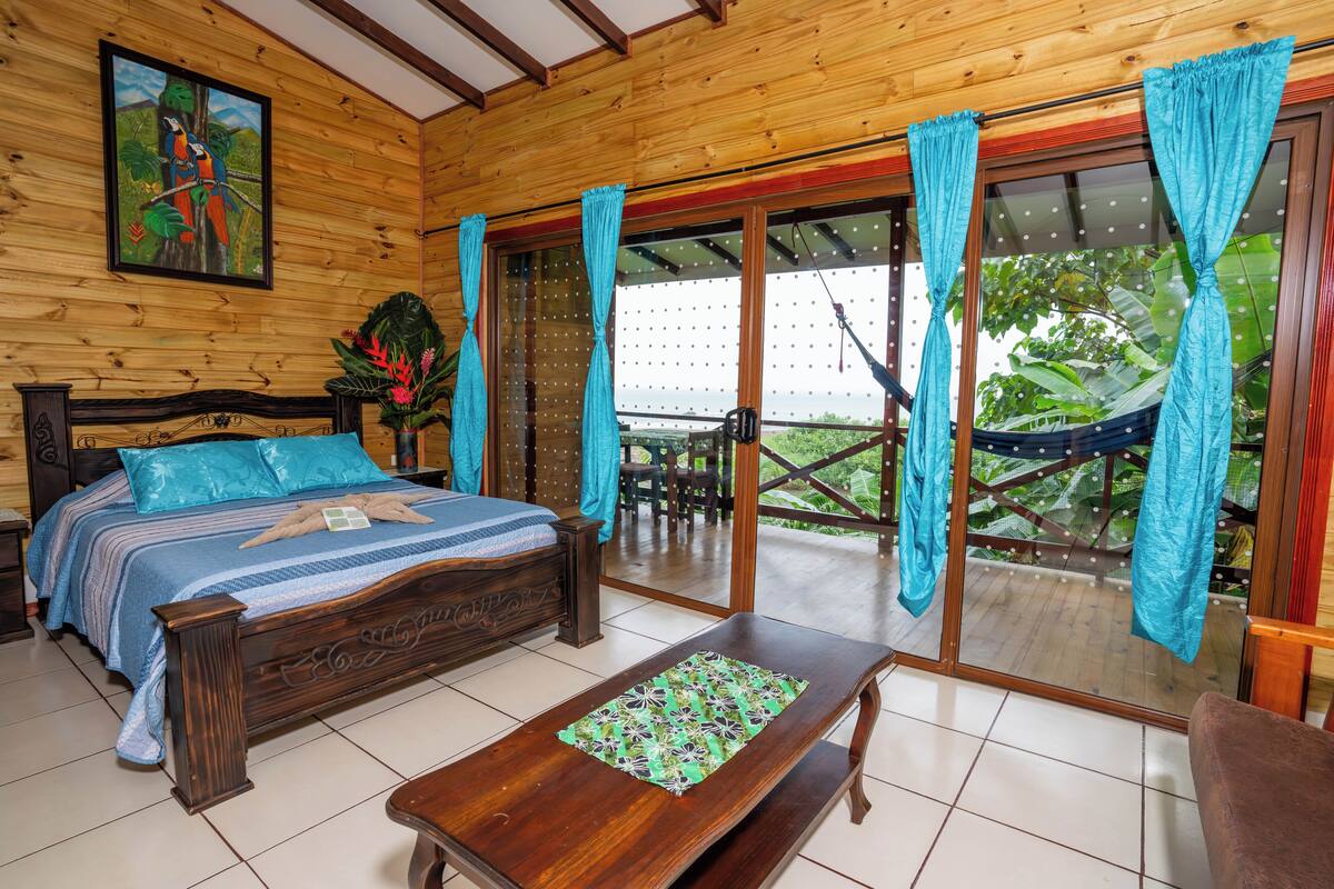 A wooden room with a bed, a bench, and a view of a garden through a sliding door.