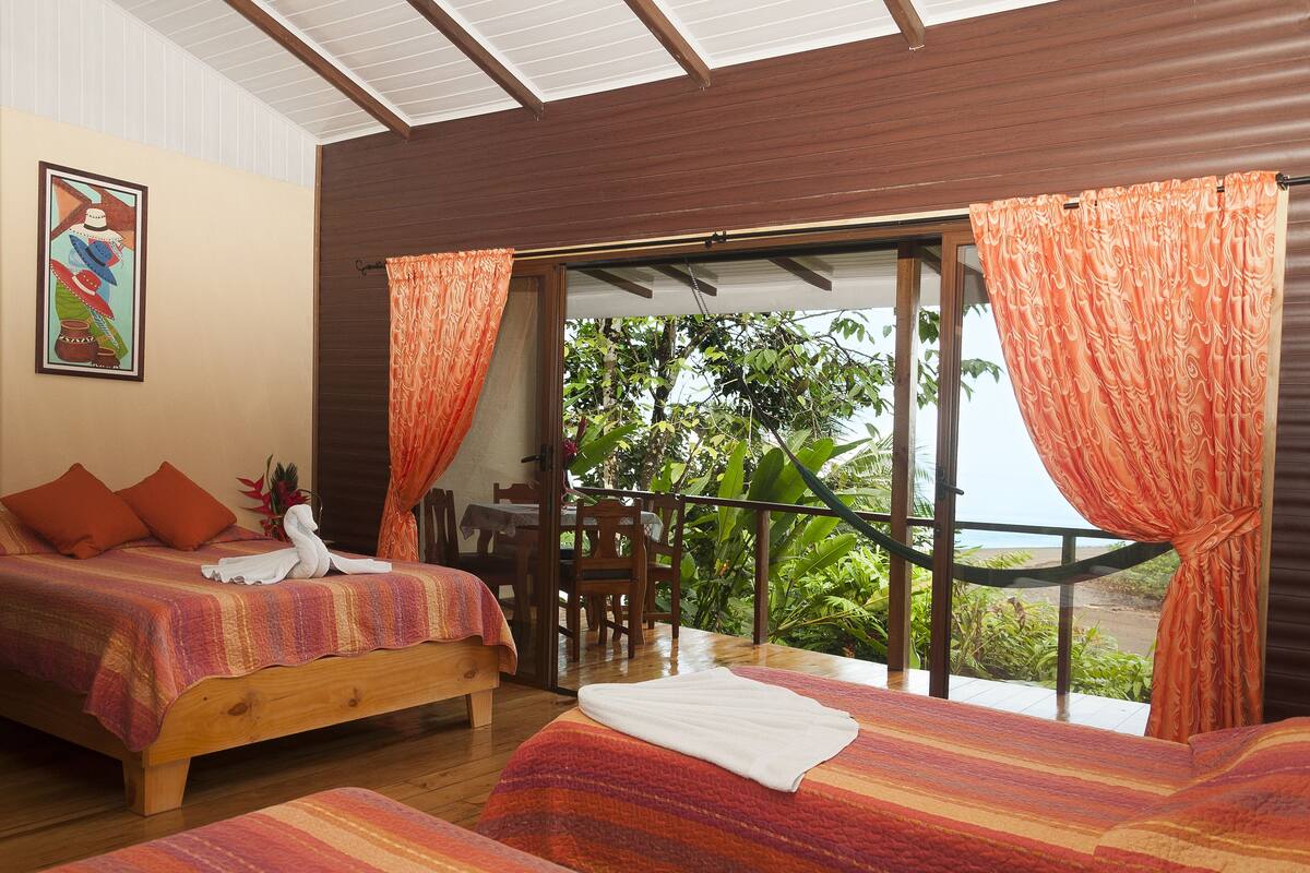 A bedroom with two beds, a wooden headboard, and a balcony with orange curtains.