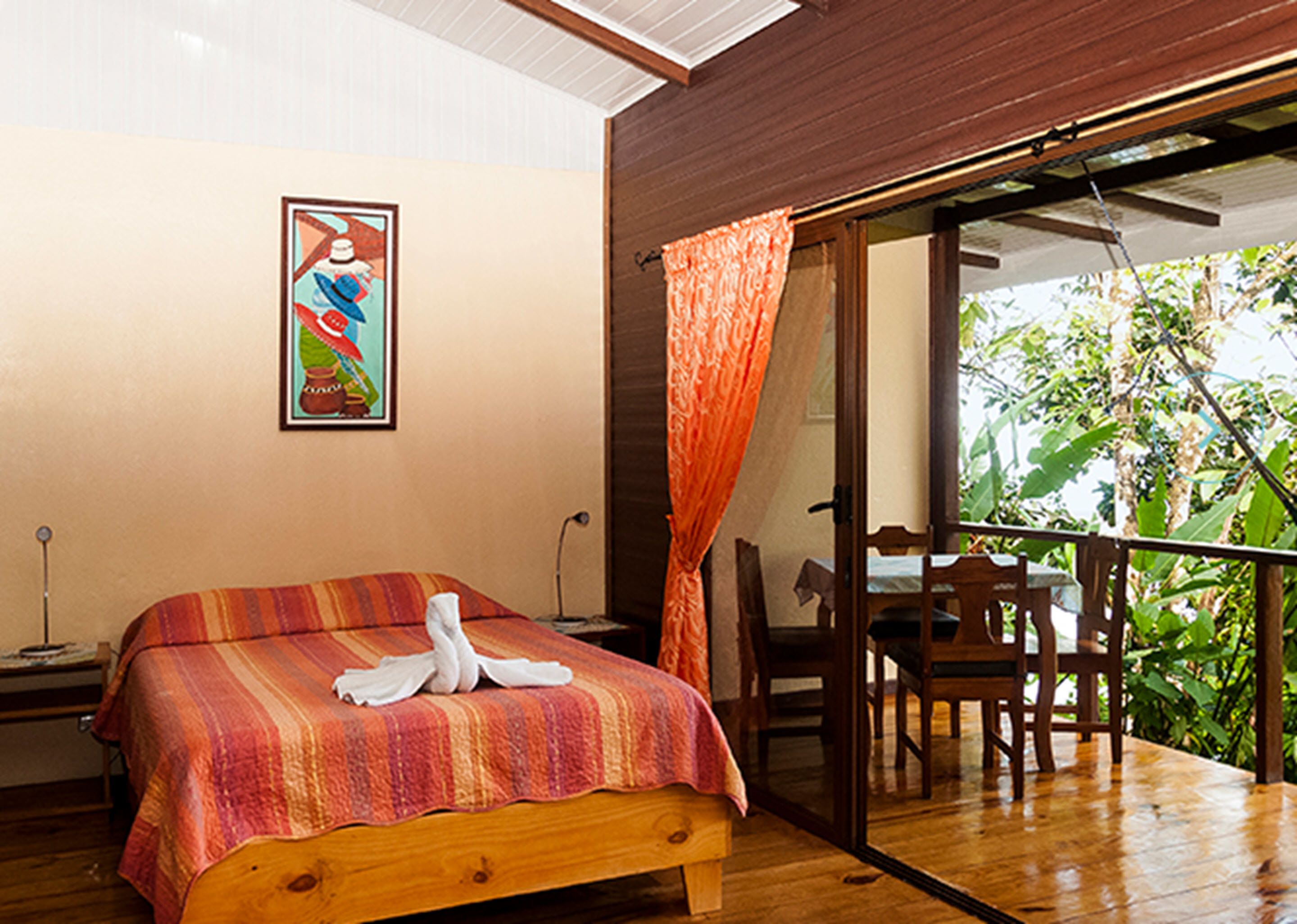 Quarto com cama, um quadro na parede e varanda com vista para o verde.