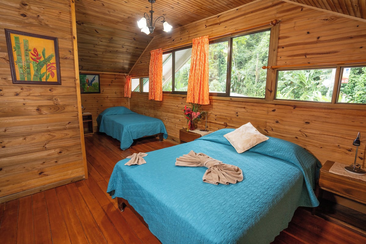 A wooden cabin room with two beds, a wooden ceiling, and large windows.