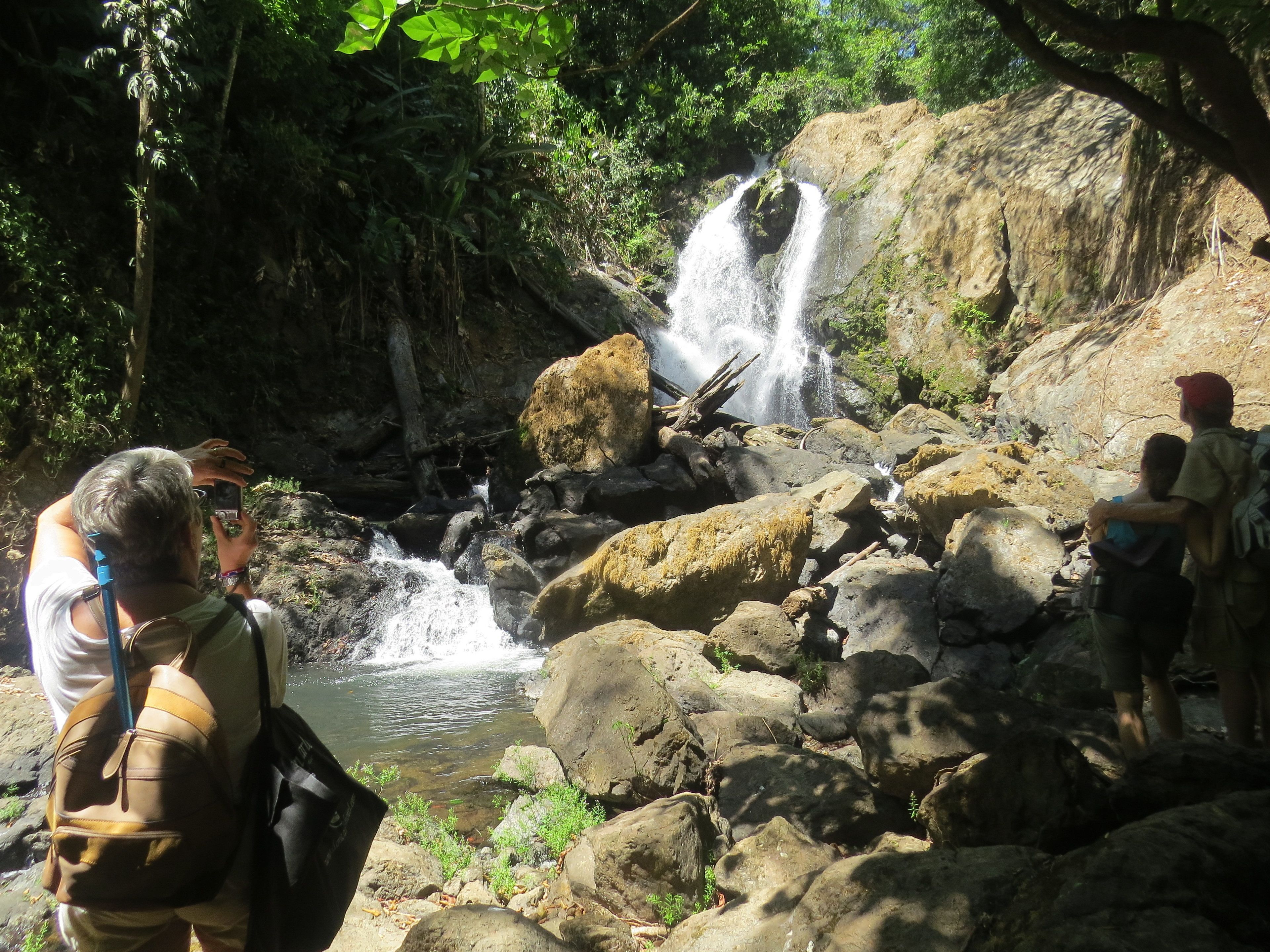 Una cascada rodeada de rocas y follaje, con gente observándola.