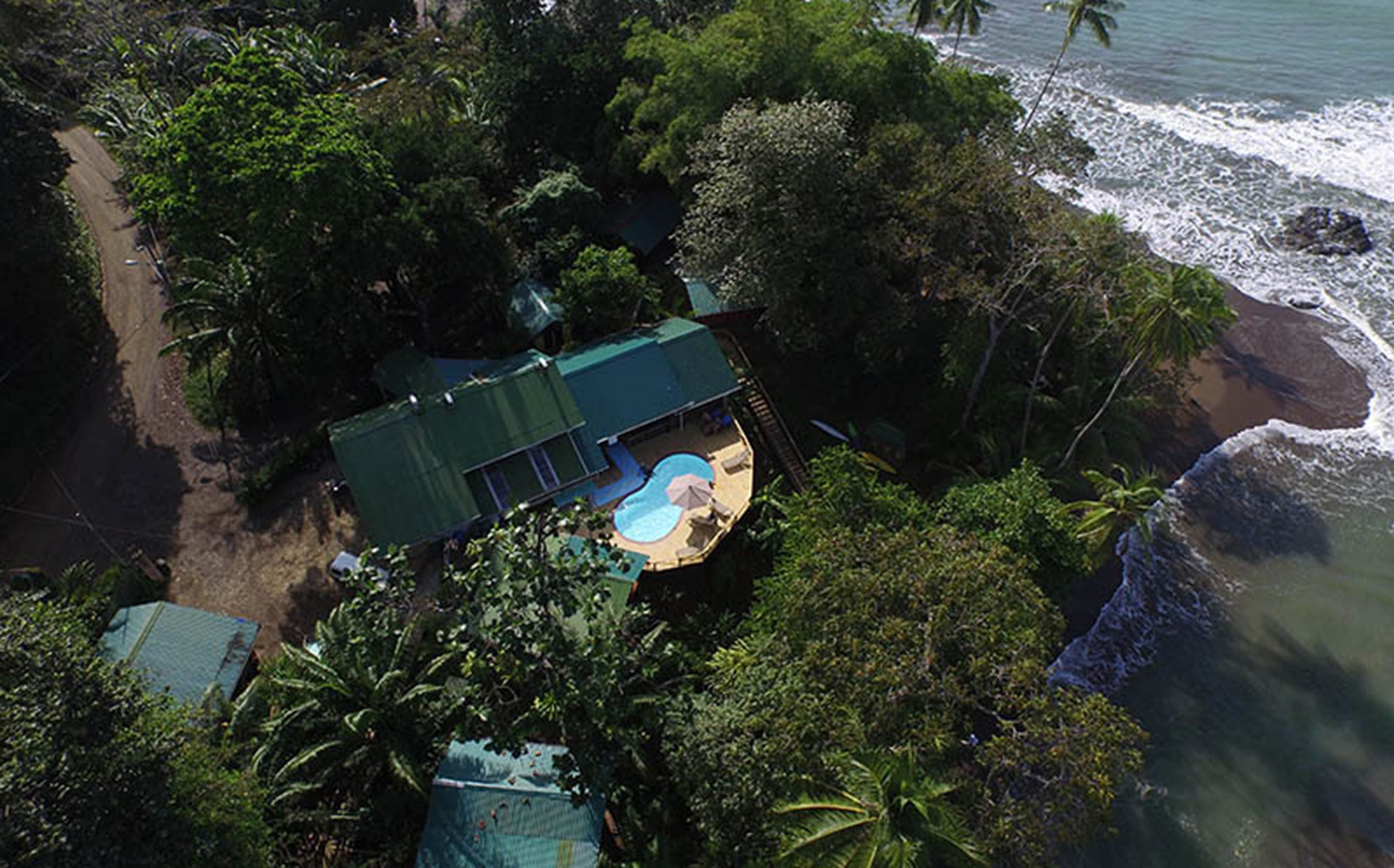 Une vue aérienne d’une maison avec une piscine, entourée d’une végétation luxuriante et donnant sur une plage.