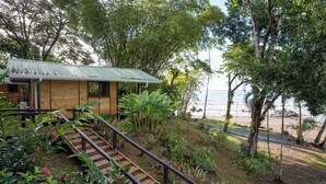 A wooden cabin with a metal roof, surrounded by lush greenery and a beach view. - Pirate Cove (Drake Bay)