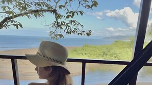 A person relaxing in a hammock on a wooden deck with a view of the beach and ocean. - Pirate Cove (Drake Bay)