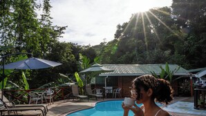 A poolside area with a glass table, lounge chairs, and umbrellas. - Pirate Cove (Drake Bay)