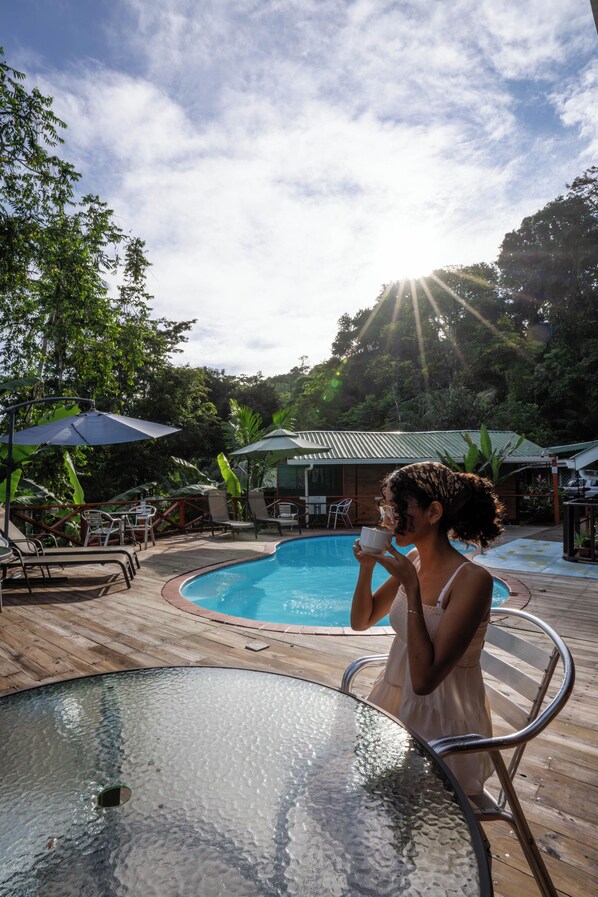 A poolside area with a glass table, lounge chairs, and umbrellas. - Pirate Cove (Drake Bay)