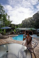 Un área junto a la piscina con una mesa de vidrio, sillas de descanso y sombrillas.