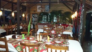 Restaurante com mesas e cadeiras de madeira, decorado com toalhas de mesa festivas e plantas.