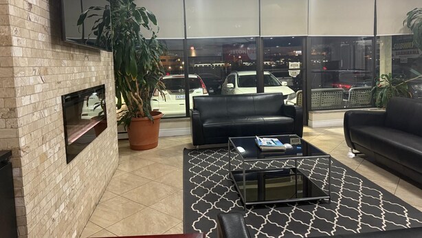 A modern lounge area with a fireplace, comfortable seating, and large windows offering a view of the street. - Nu Hotel Toronto (Mississauga)