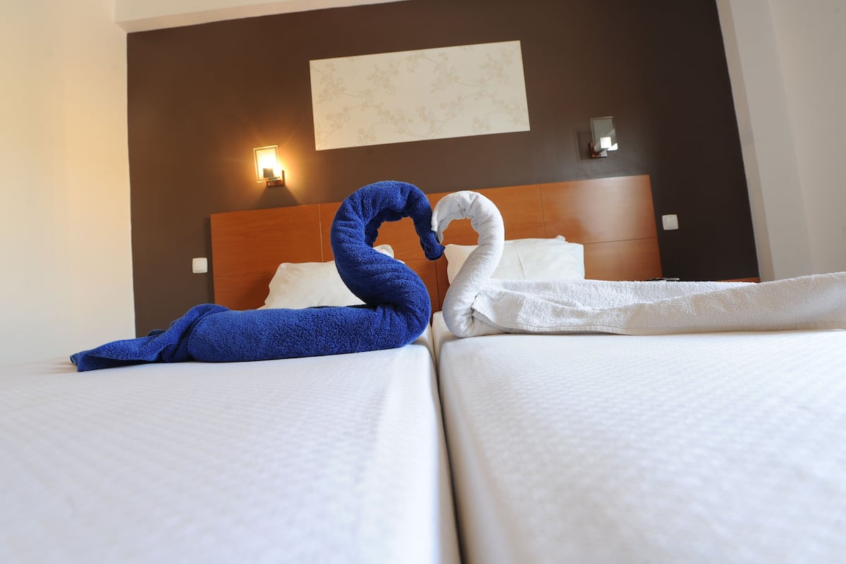 A hotel room with two beds, a wooden headboard, and wall-mounted lights.