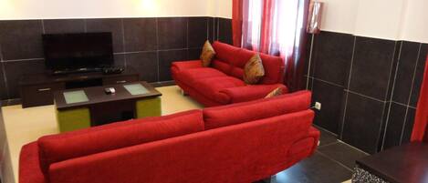 Una sala de estar con un sofá rojo, un televisor de pantalla plana y una mesita.