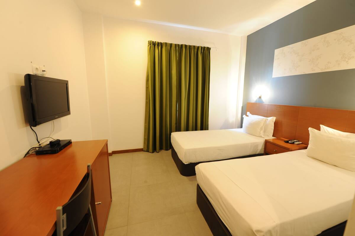 A hotel room with two beds, a desk, a television, and a curtain.