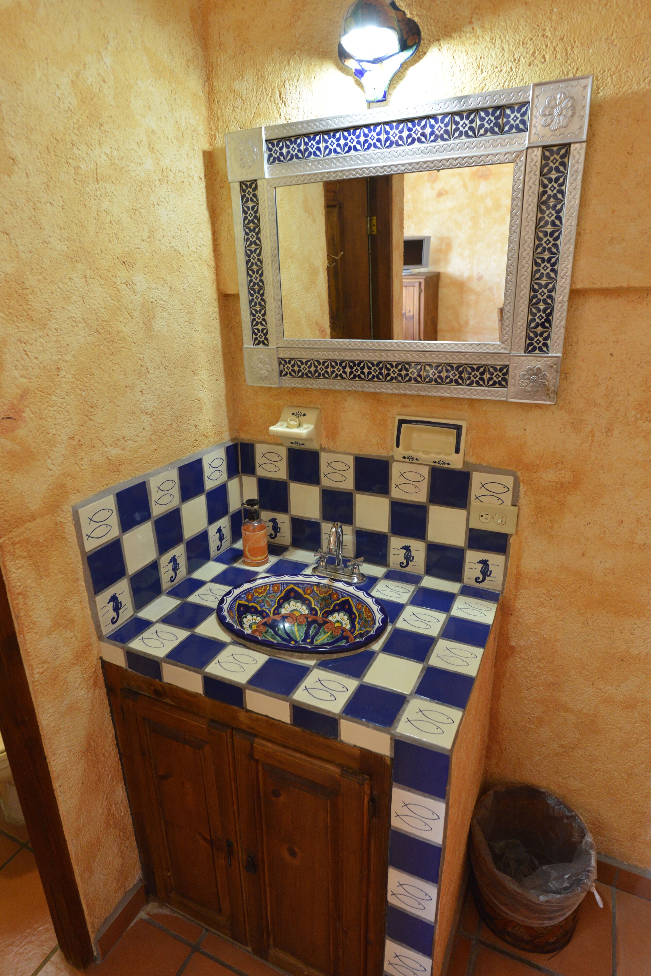 A bathroom with a checkered tile sink, a mirror with decorative frame, and a wooden cabinet.