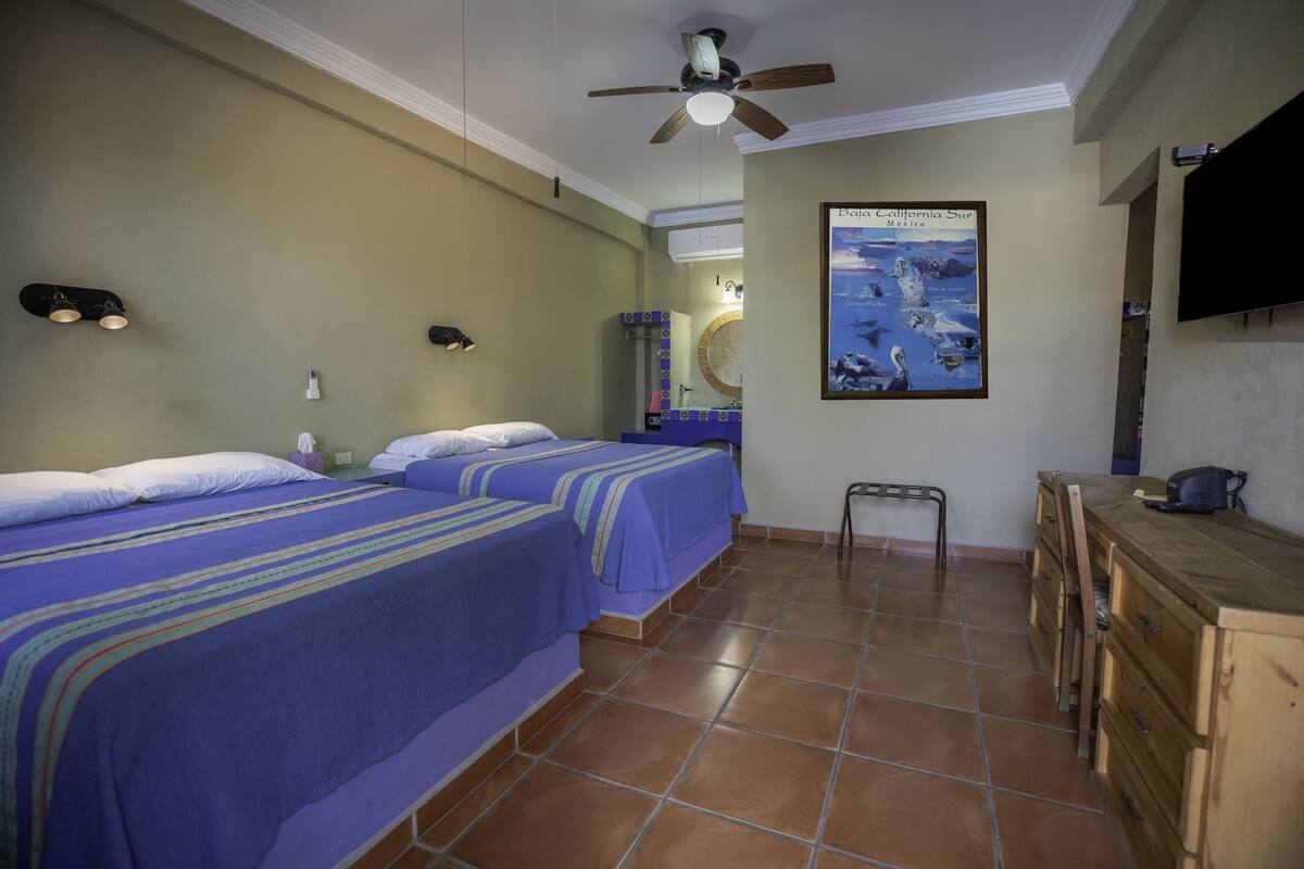 A hotel room with two beds, a ceiling fan, a bathroom mirror, a wooden dresser, and a poster on the wall.