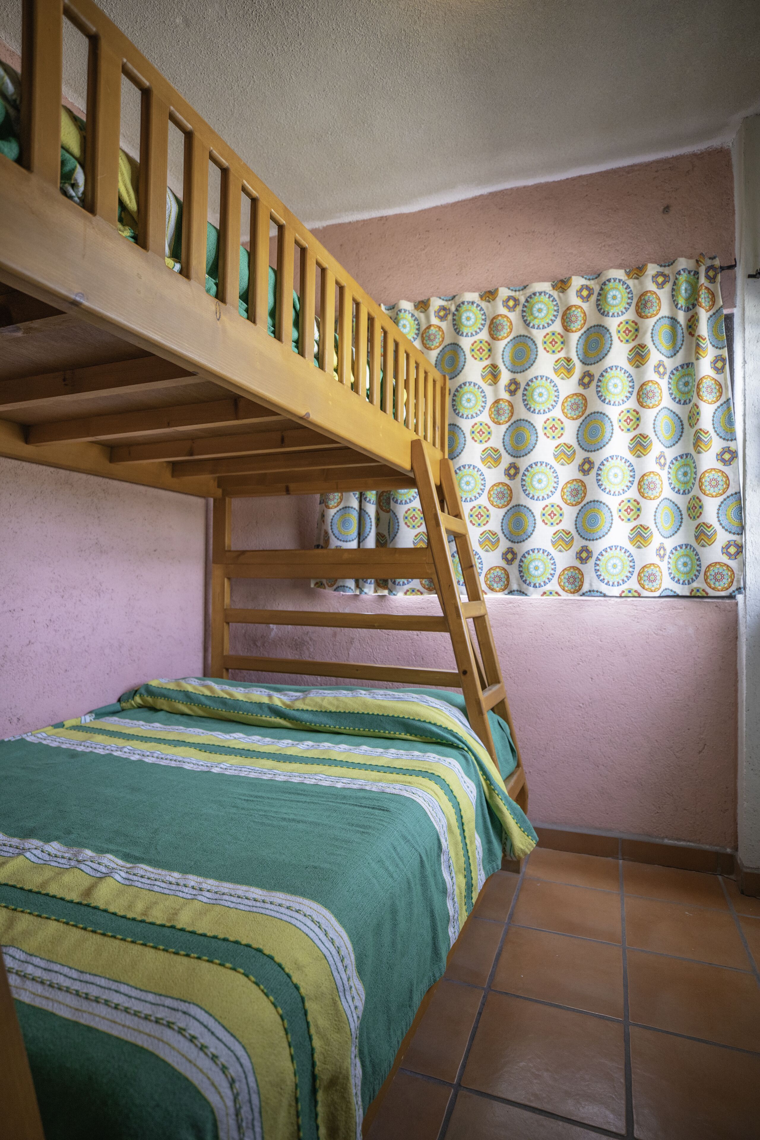 Una cama litera con una escalera de madera, una colcha a rayas verdes y blancas, y una cortina estampada.